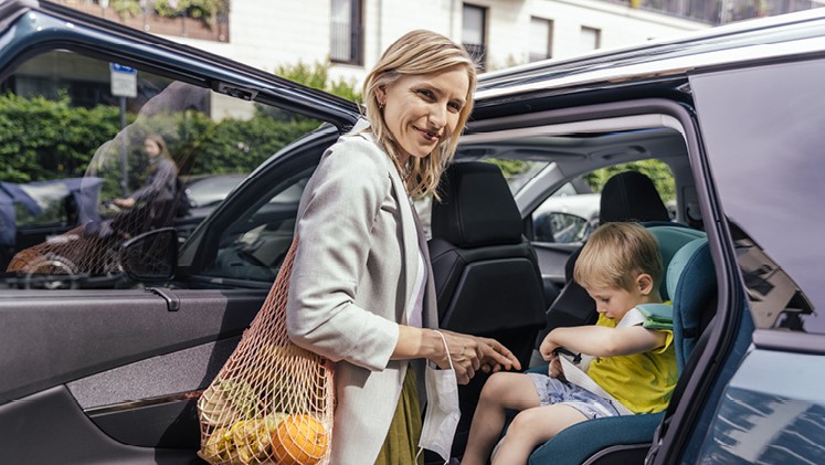Frau schnallt ein Kind im Autositz an 