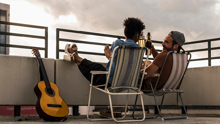 Junge Leute sitzen mit Bier und Gitarre auf Dachterrasse